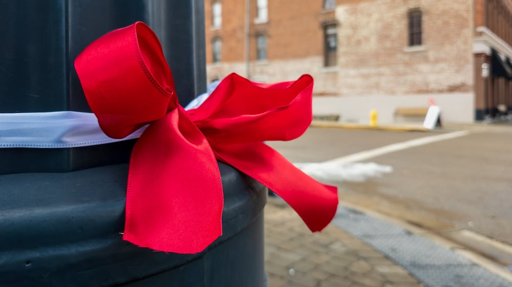 Red and white ribbons tied with bows have been attached to traffic poles, lampposts and trees along Main Street in Tipp City’s downtown historic district in memory of Ashley Flynn, a 37-year-old mother of two who was fatally shot during a reported home burglary early on Monday, Feb. 16. Area residents said on Wednesday the crime has shocked the close-knit community. BRYANT BILLING / STAFF