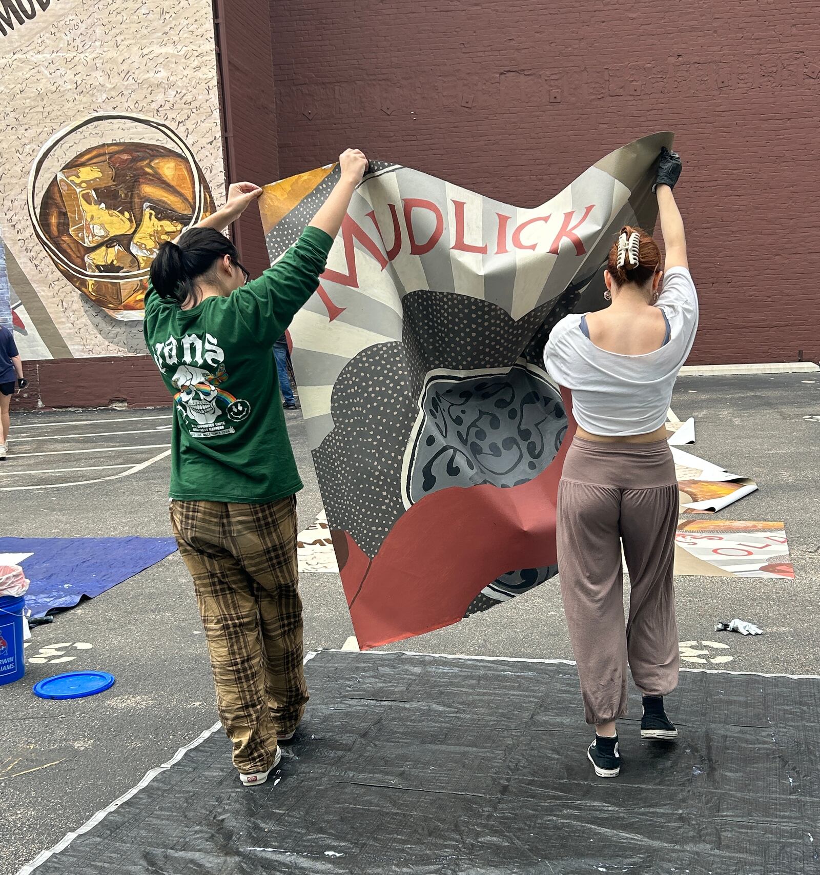 Archer Yuan and Mia Masic carry a panel of the mural over to the side of Mudlick Tap House to be pasted in place. STAFF/ZOE HILL