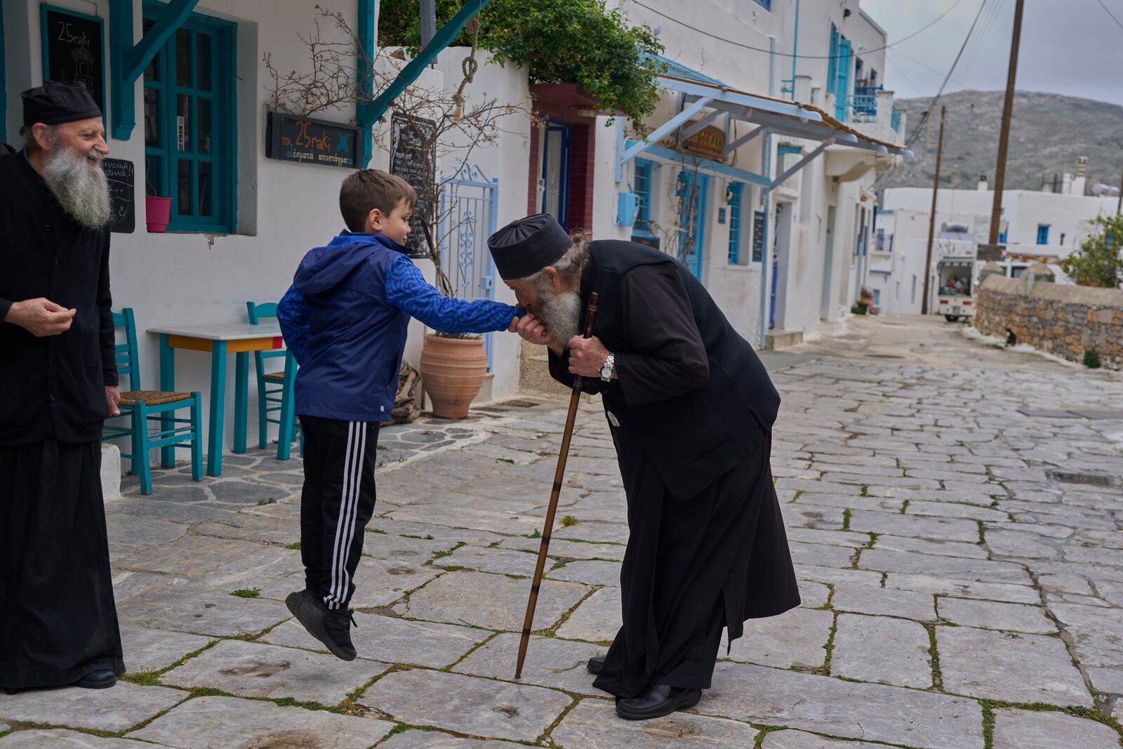 Orthodox Christian monk Father Spyridon of Amorgos, kisses the hand of the son of his nephew Nikitas Vasalos as father Kostas looks on, in Lagada village, Amorgos island, Greece, on Saturday, March 29, 2025.(AP Photo/Petros Giannakouris)