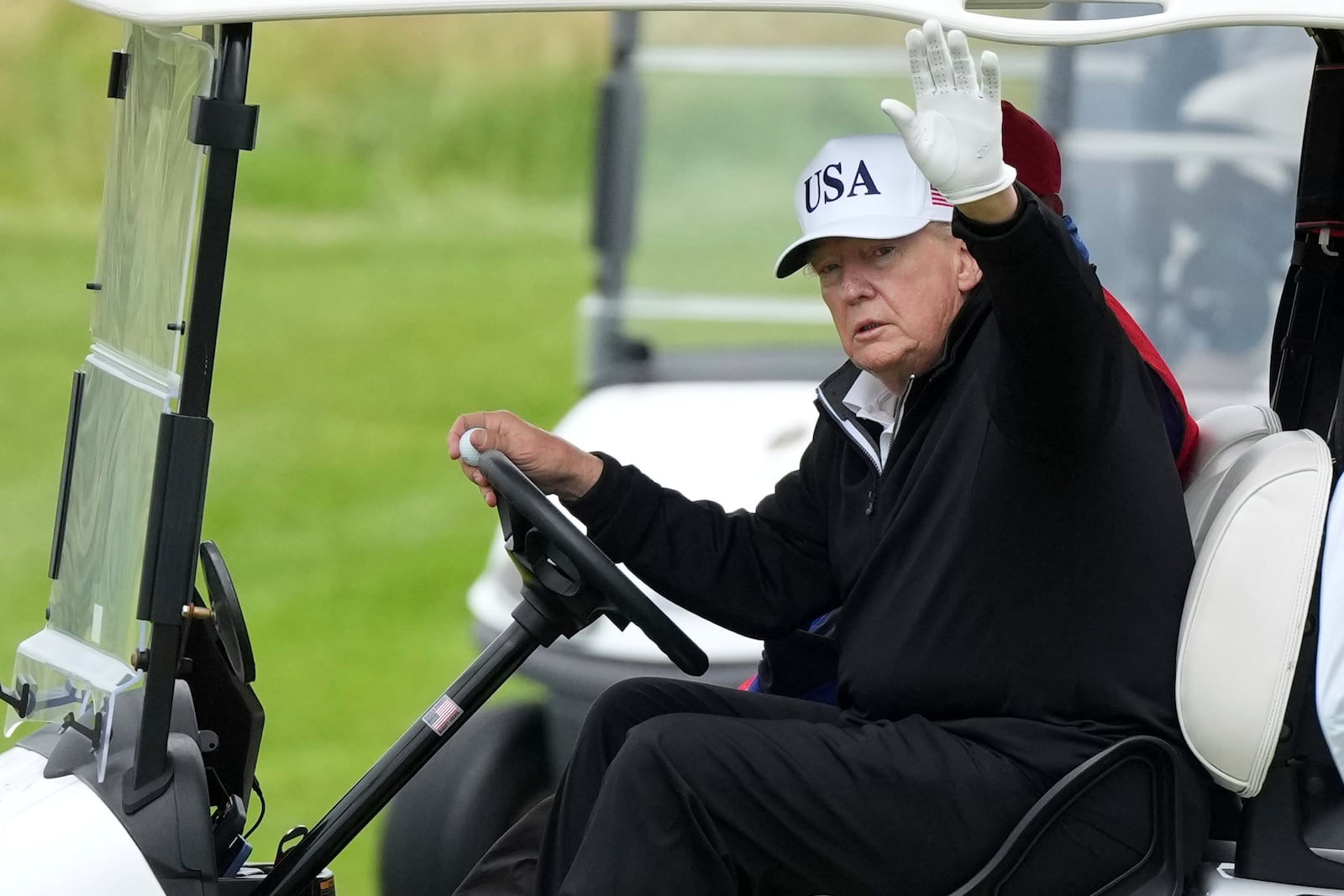 President Donald Trump waves to reporters as he steers his golf cart at the Trump Turnberry golf course in Turnberry, Scotland, Sunday, July 27, 2025.(AP Photo/Alastair Grant)