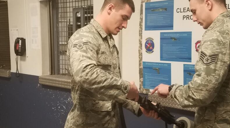 Airman 1st Class Joshua Campbell shows how to turn in a weapon to Senior Airman Alec Brennan, who is standing behind the armory window at the 88th Security Forces Armory, Bldg. 295, Area A. (U.S. Air Force photos/Laura McGowan)