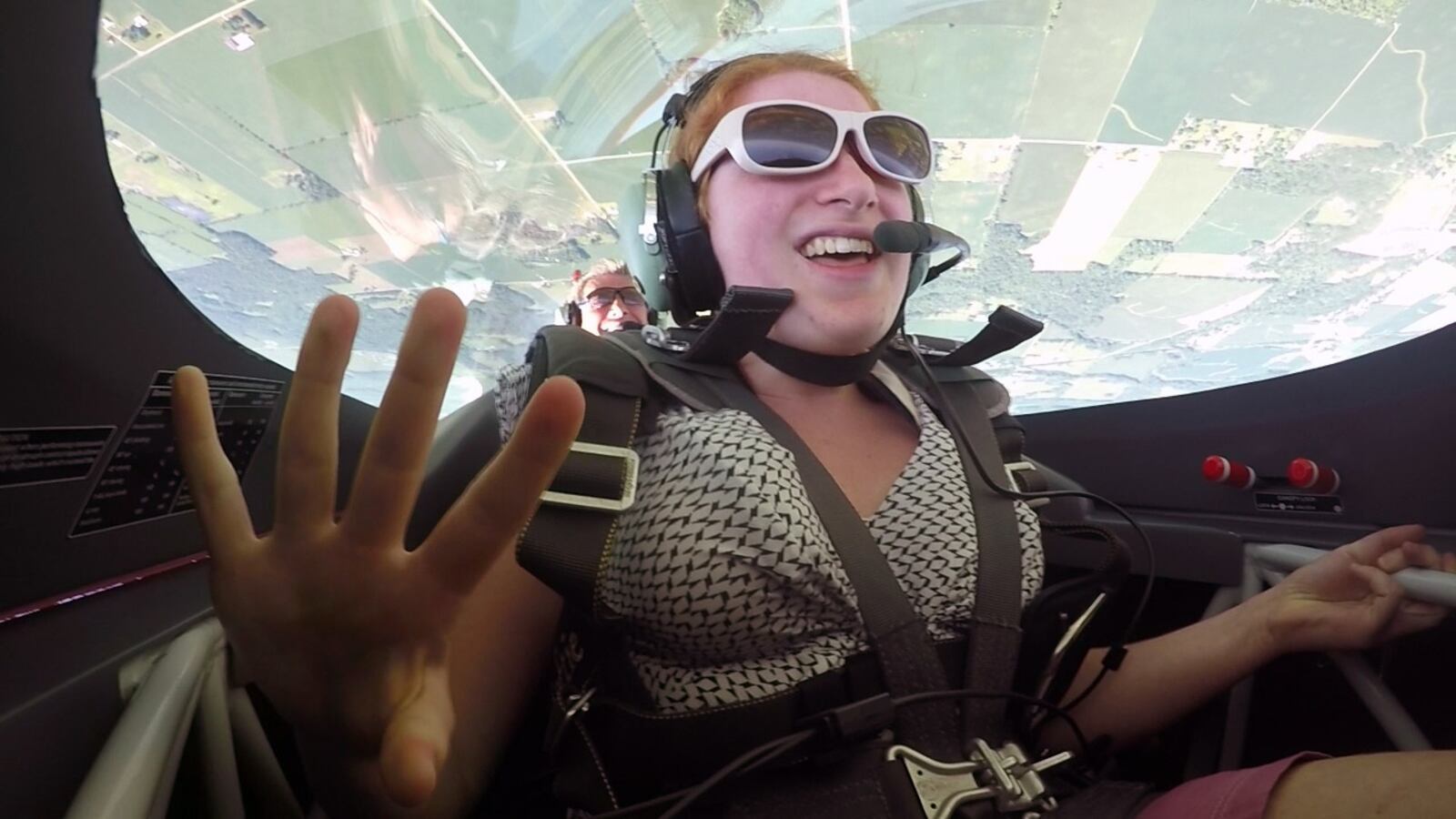 Dayton Air Show Young Eagles essay contest winner Kayla Hughes, 14, waves from the front seat of an aerobatic airplane piloted by legendary pilot Sean D. Tucker in the skies over Miami County.  Hughes originally scheduled flight was cancelled due to poor weather days before the Dayton Air Show in June but Tucker found a way to make it happen on Tuesday in Piqua.   TY GREENLEES / STAFF
