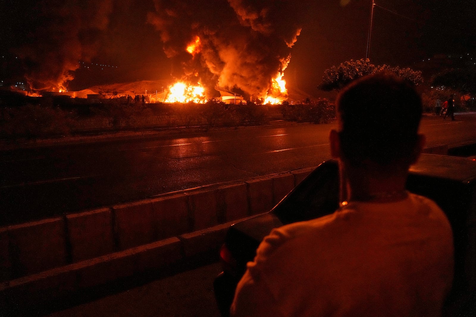 A man looks at blazes of the oil storage after it was hit by an Israeli strike in Tehran, Iran, early Sunday, June 15, 2025. (AP Photo/Vahid Salemi)
