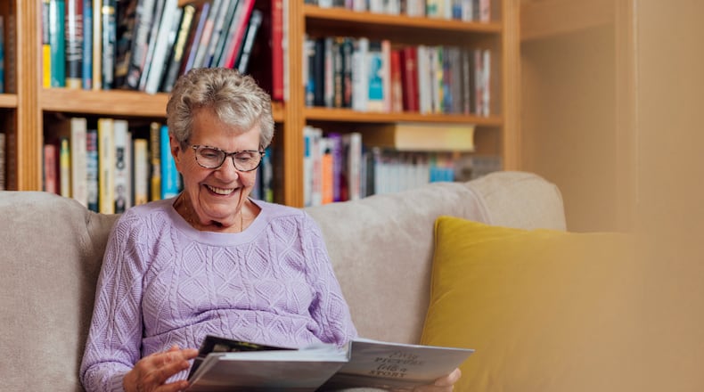 A senior woman with dementia looks through a photo album to aid her memory and remind her of the relationships she has with people in the book. iSTOCK/COX