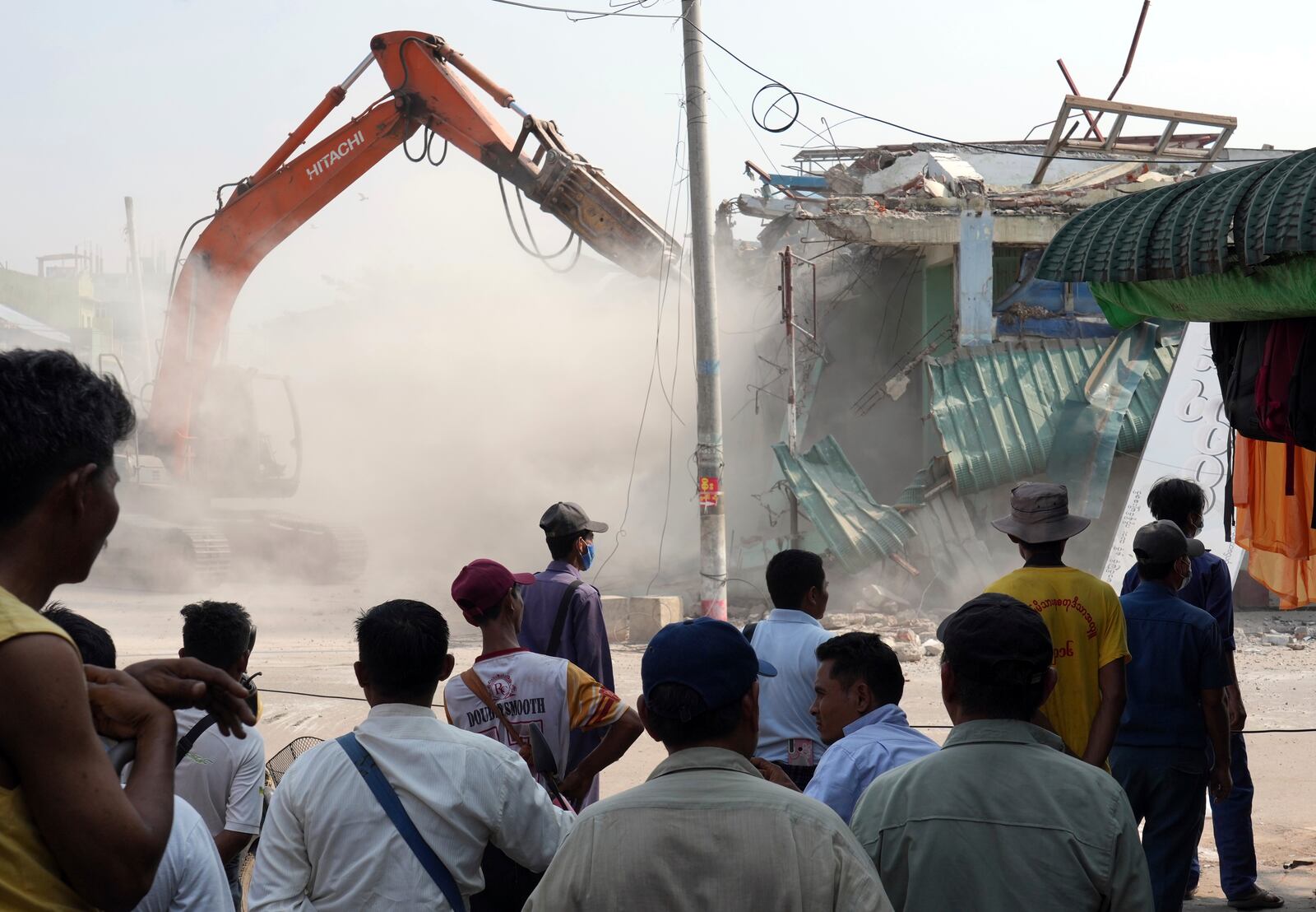 People watch as a backhoe clear debris from damaged buildings at a market, after one month of the strong earthquake in Naypyitaw, Myanmar, Monday, April 28, 2025. (AP Photo/Aung Shine Oo)