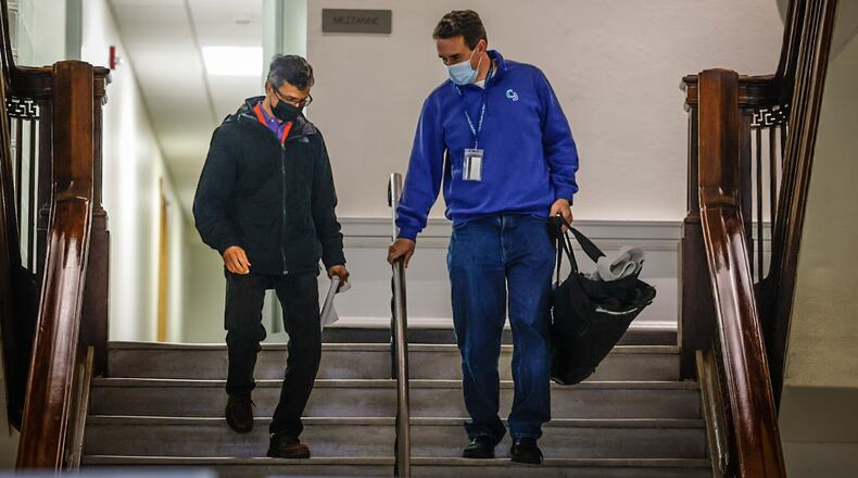 Two City of Dayton employees walk down steps from the mezzanine level at city hall Friday January 6, 2023. The city of Dayton is requiring all employees to wear masks at work due to elevated local COVID levels. JIM NOELKER/STAFF