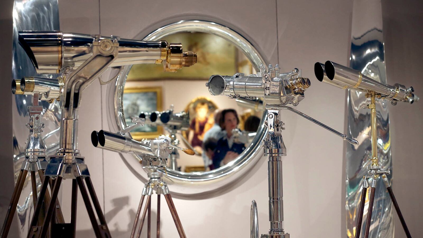 A visitor to the Palm Beach Jewelry, Art and Antique Show is reflected on a mirror near World War II polished aluminum binoculars at the Daniels gallery booth Feb 16, 2015, at the Palm Beach County Convention Center in West Palm Beach. (Bill Ingram / Palm Beach Post)