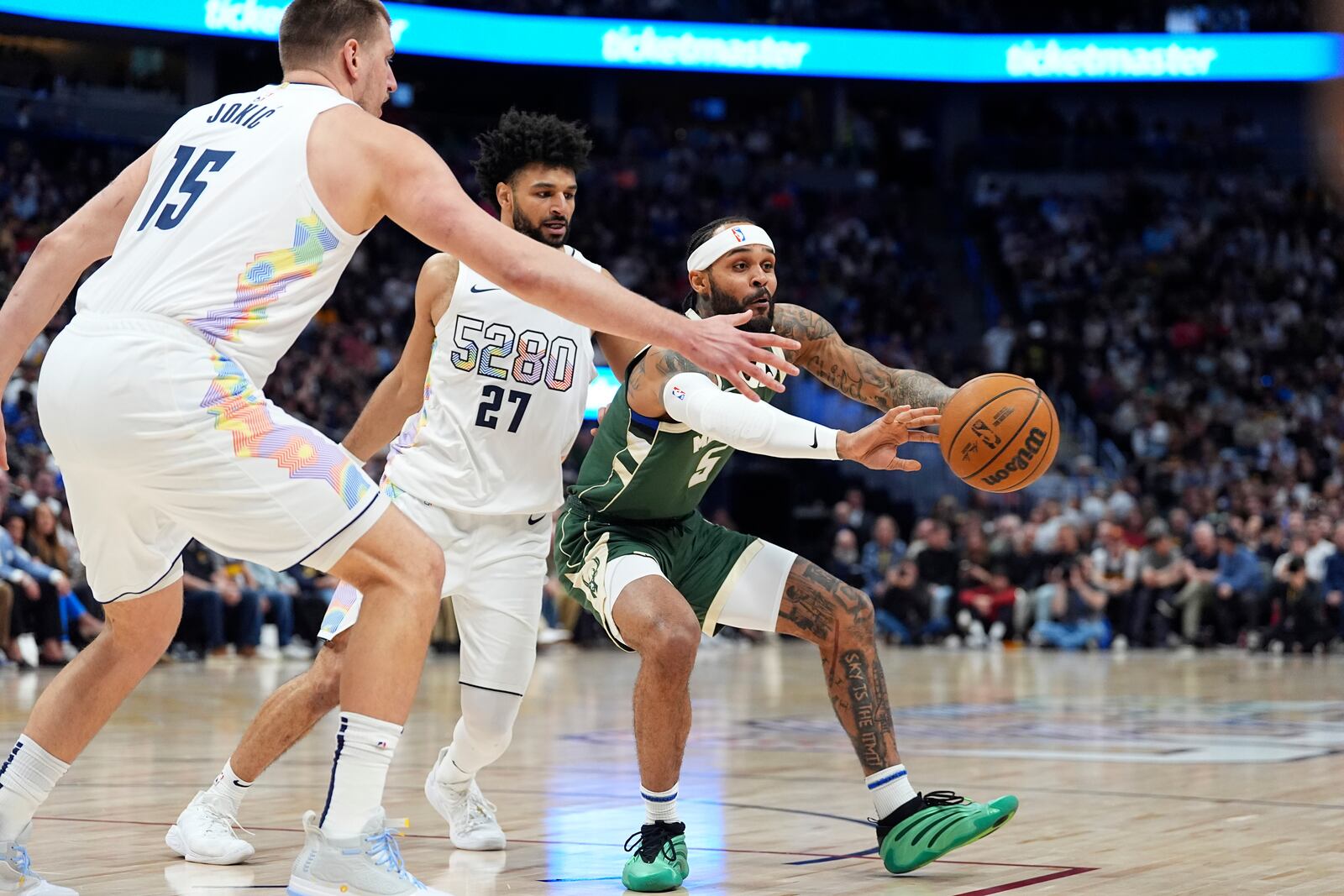 Milwaukee Bucks guard Gary Trent Jr., right, passes the ball as Denver Nuggets guard Jamal Murray and center Nikola Jokic, left, in the first half of an NBA basketball game Wednesday, March 26, 2025, in Denver. (AP Photo/David Zalubowski)