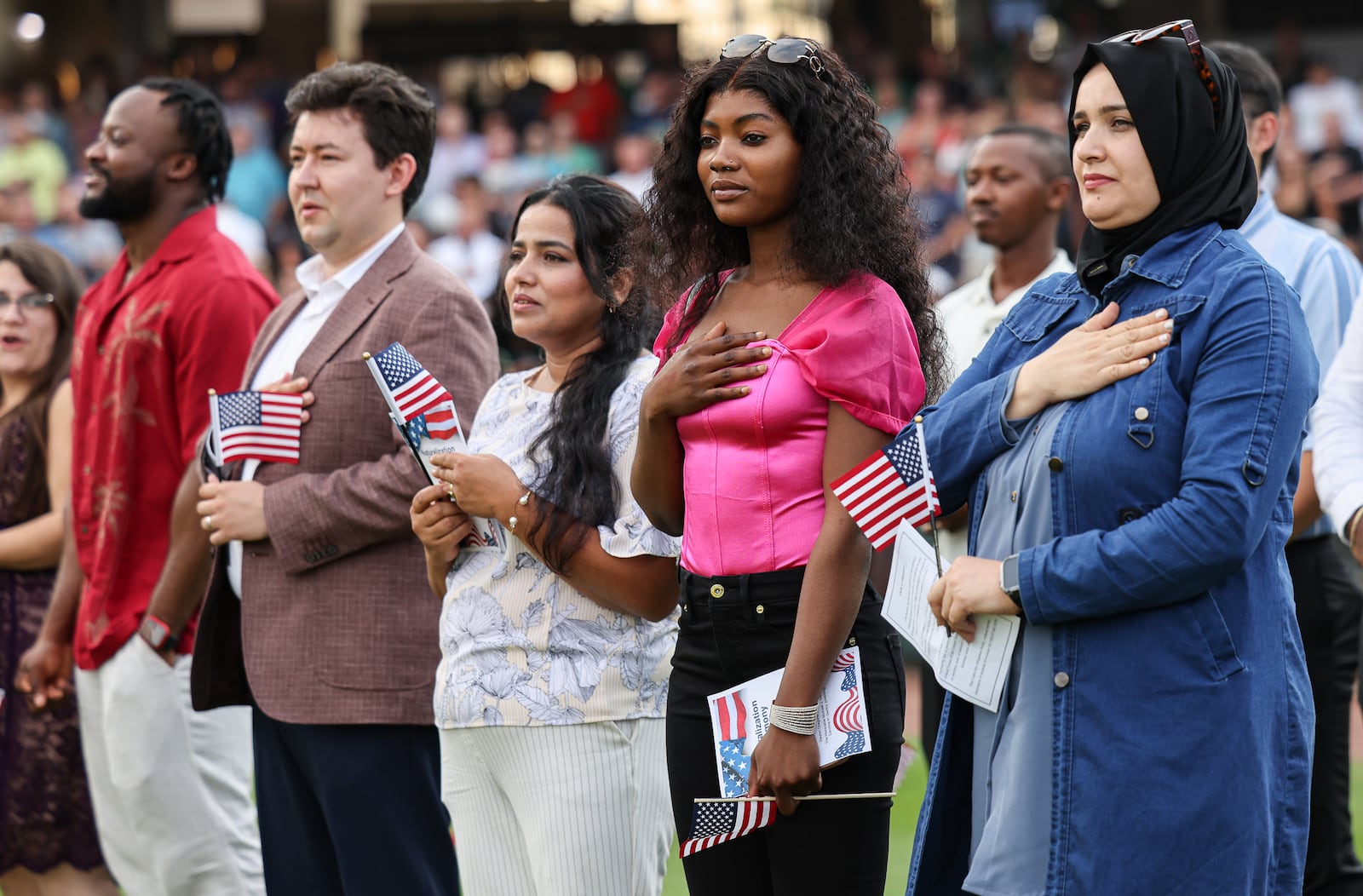 Twenty immigrants became U.S. citizens during a naturalization ceremony on Tuesday, Aug. 5, between the third and fourth innings during a Dayton Dragons game at Day Air Ballpark, including Aziza Yenga (center right, in pink) who immigrated from Tanzania. BRYANT BILLING / STAFF