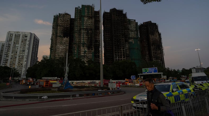 A man walks past charred buildings burnt after a deadly fire that started Wednesday at Wang Fuk Court, a residential estate in the Tai Po district of Hong Kong's New Territories, Friday, Nov. 28, 2025. (AP Photo/Ng Han Guan)