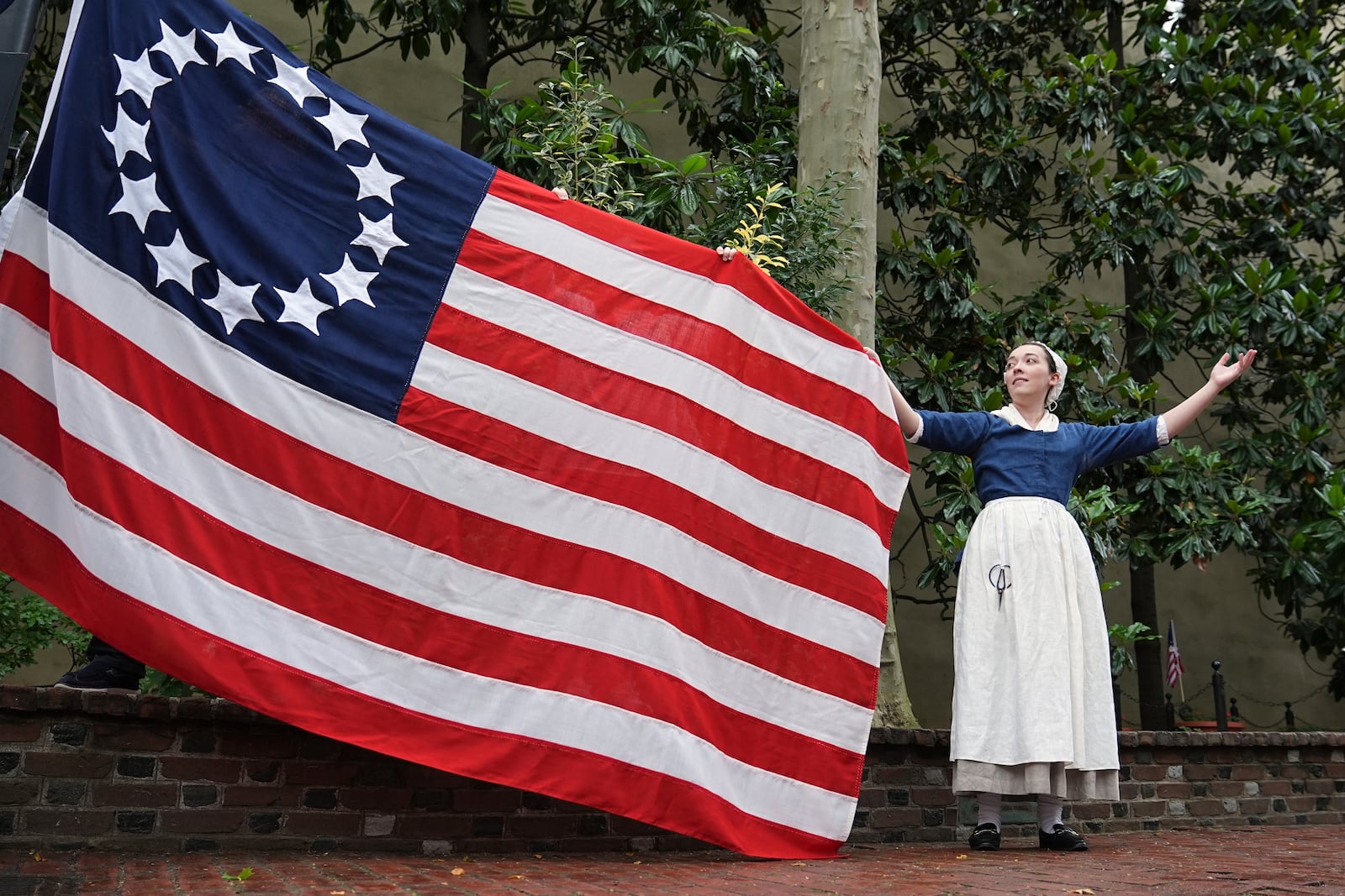 Madeline Burk, portraying Betsy Ross, holds a flag as it is hoisted up at the Betsy Ross House in Philadelphia, Monday, June 9, 2025. (AP Photo/Matt Rourke)