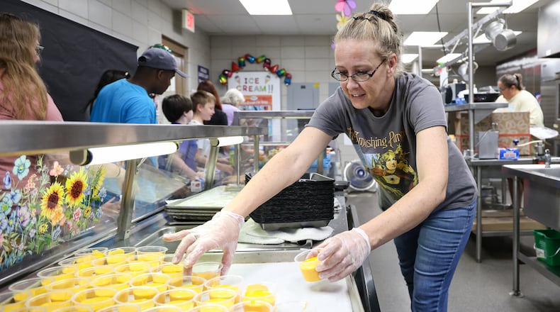 Amber Bowling, a food and nutrition worker, grabs cups of cheese sauce to put out for children to eat on Friday, Aug. 1 during a summer lunch program at Greenmont Elementary School in Kettering. Kettering City Schools organized the summer lunch program, which ran from June 2 to Friday. BRYANT BILLING / STAFF