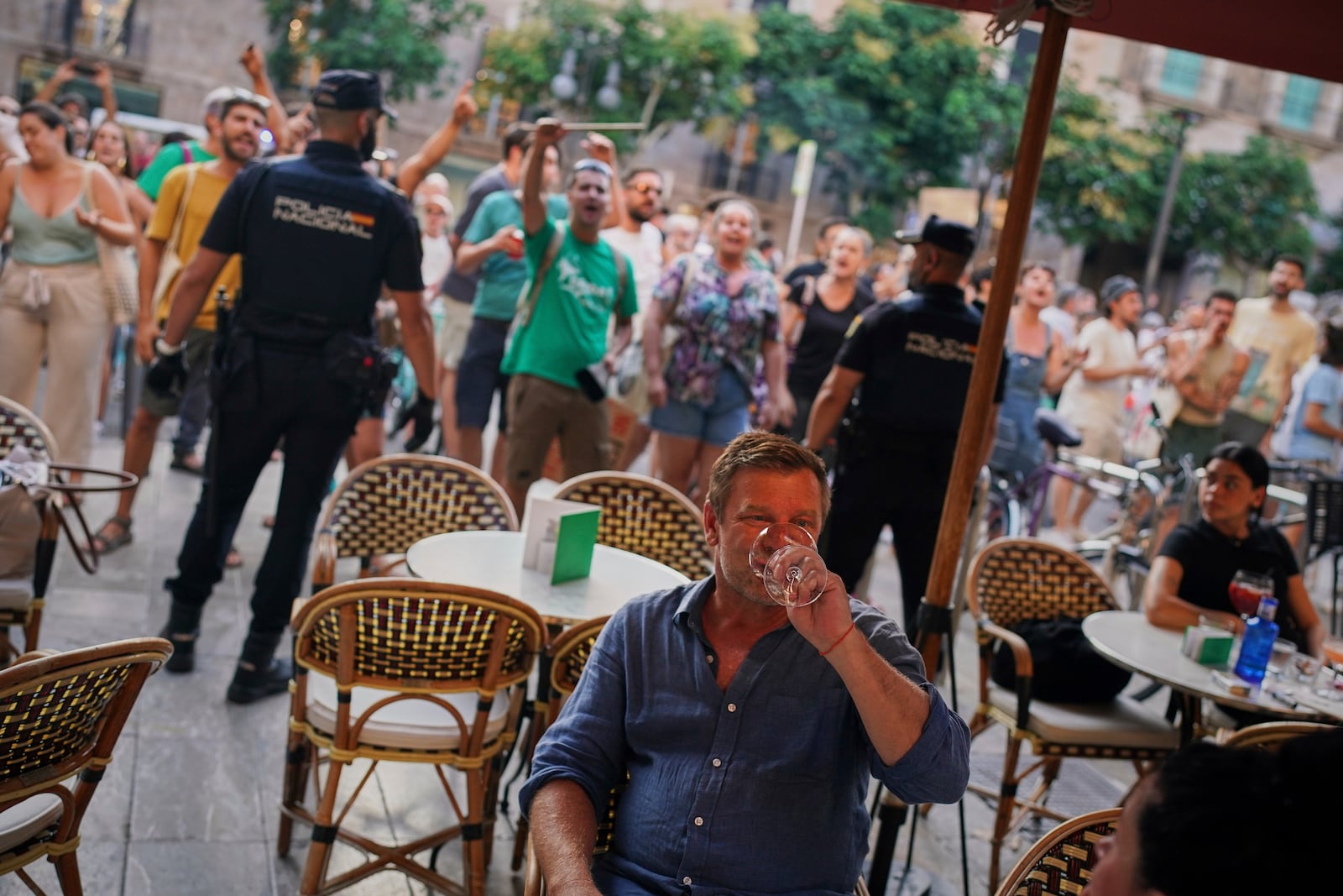 Tourists sit in a restaurant as people protest against overtourism in the Balearic island of Mallorca, Spain, Sunday, June 15, 2025. (AP Photo/Joan Mateu Parra)