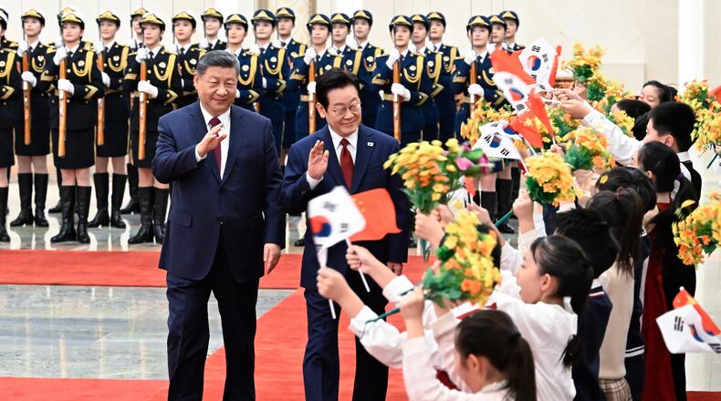 In this photo released by Xinhua News Agency, visiting South Korean President Lee Jae Myung, center, and Chinese President Xi Jinping is welcomed by children waving both countries national flags and flowers after inspecting a guard of honor during a welcoming ceremony at the Great Hall of the People, in Beijing, Monday, Jan. 5, 2026. (Shen Hong/Xinhua via AP)