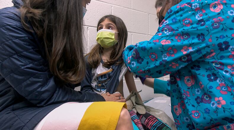 In this Wednesday, March 24, 2021 image from video provided by Duke Health, Alejandra Gerardo, 9, looks up to her mom, Dr. Susanna Naggie, as she gets the first of two Pfizer COVID-19 vaccinations during a clinical trial for children at Duke Health in Durham, N.C. In the U.S. and abroad, researchers are beginning to test younger and younger kids, to make sure the shots are safe and work for each age. (Shawn Rocco/Duke Health via AP)