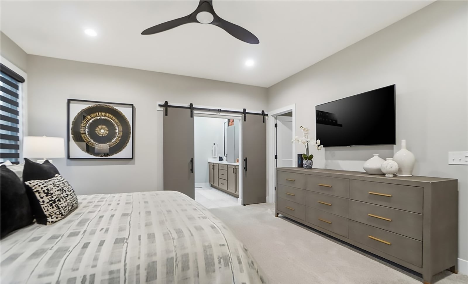 The first floor primary bedroom suite has neutral carpeting, a ceiling fan and an ensuite bathroom with barn doors. CONTRIBUTED