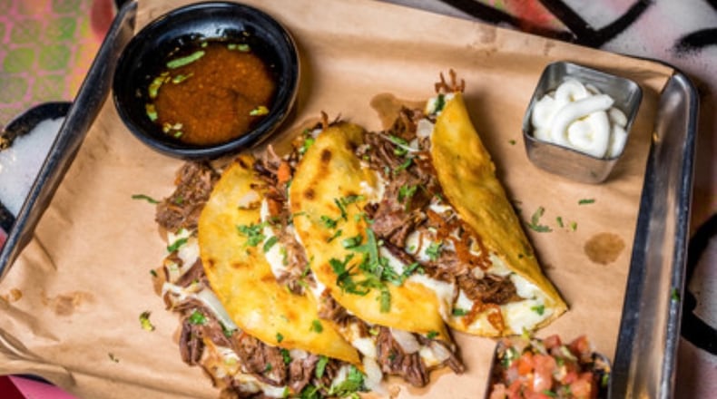The Birria, three Slow-Braised Beef with Guajillo Chilies, Oaxaca Cheese, Cilantro, Onion, Dipping Consommé.