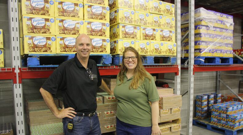 Mike Burke and Jamie Dailey stand next to shelves of food at Ahler’s Catering’s Vandalia warehouse that will be sorted and delivered to clients around the Miami Valley. KAITLIN SCHROEDER