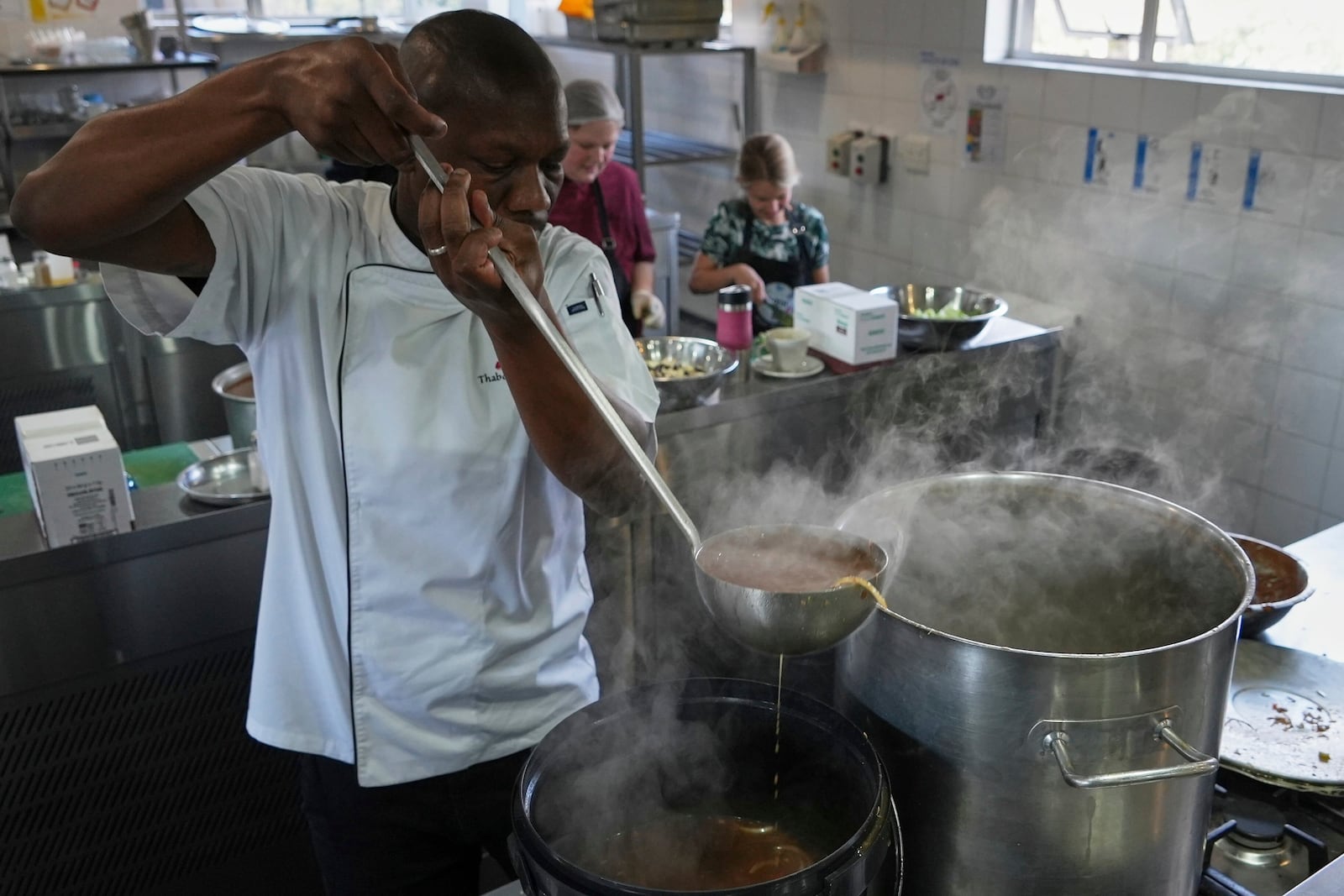 Chef Thabo Letsholo, uses a ladle spoon to fill the bucket with soup as part of chefs, community cooks, caterers, and culinary students joined forces to whip together 67,000 litres of soup in celebration of Nelson Mandela Day in Johannesburg, South Africa, Friday, July 18, 2025. (AP Photo/Alfonso Nqunjana)