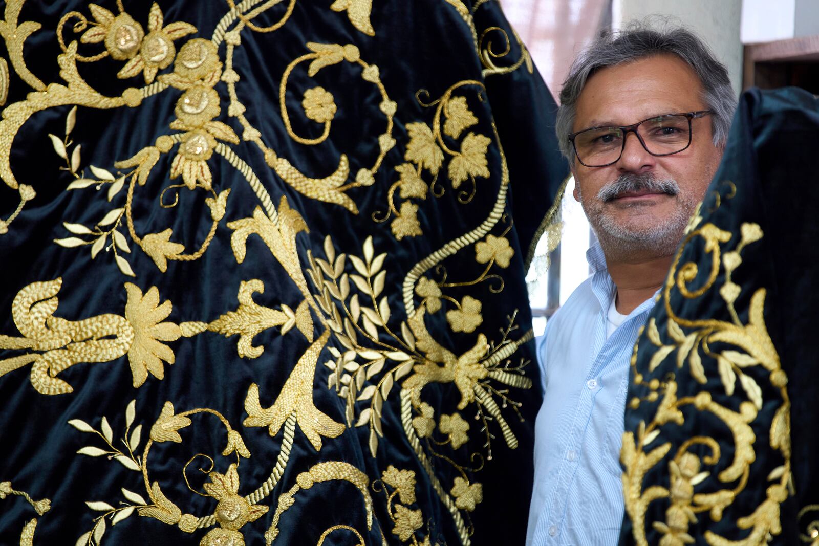 Guatemalan artist Alejandro Juarez poses with his finished tunic to be worn by a statue of the Virgin Mary, at the Maria Auxiliadora embroidery workshop in San Miguel Escobar, Guatemala, Wednesday, April 2, 2025. (AP Photo/Moises Castillo)