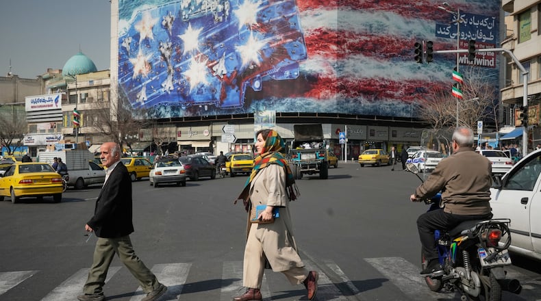 Pedestrians walk past a billboard depicting a U.S. aircraft carrier with damaged fighter jets on its deck and a sign in Farsi and English reading, "If you sow the wind, you'll reap the whirlwind," at Enqelab-e-Eslami (Islamic Revolution) Square in Tehran, Iran, Sunday, Feb. 22, 2026. (AP Photo/Vahid Salemi)
