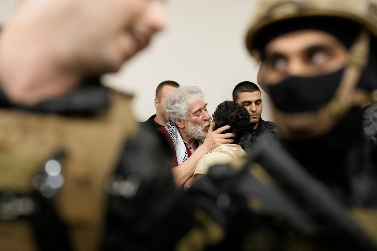 Lebanese pro-Palestinian militant Georges Abdallah, center left, who was serving a life sentence for complicity in the 1982 murders of a U.S. and an Israeli diplomat in Paris, is greeted by a supporter and surrounded by security forces upon his arrival in Qobayat village, in northern Akkar province, Lebanon, Friday, July 25, 2025. (AP Photo/Hassan Ammar)