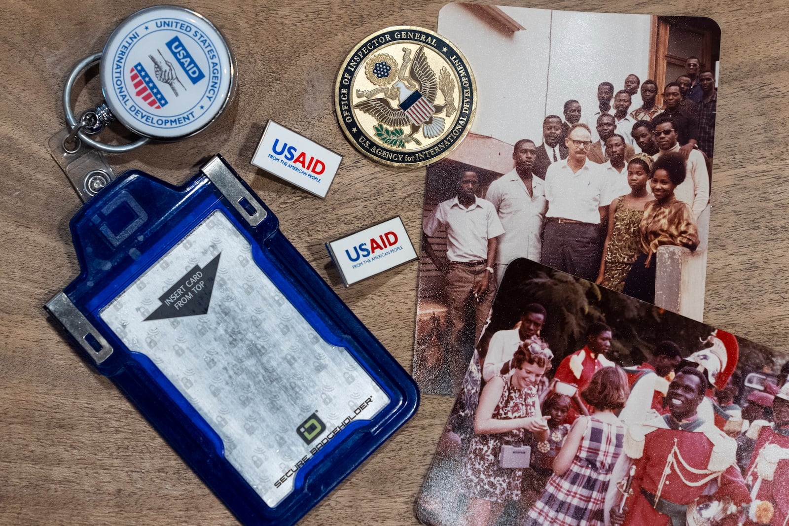 Anna Eisenberg's empty USAID badge holder is seen next to USAID pins, a coin from the USAID Office of Inspector General awarded to her mother, Cathy Votaw, and photographs of her grandfather, Albert Votaw, and his family during his service with USAID in West Africa circa 1968, Thursday, Feb. 27, 2025, in Washington. (AP Photo/Jacquelyn Martin)