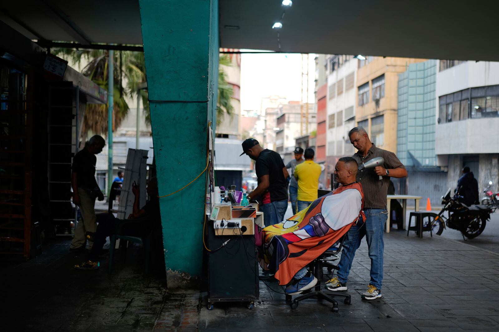 A man gets a haircut under the Fuerzas Armadas bridge in Caracas, Venezuela, Thursday, April 10, 2025. (AP Photo/Ariana Cubillos)