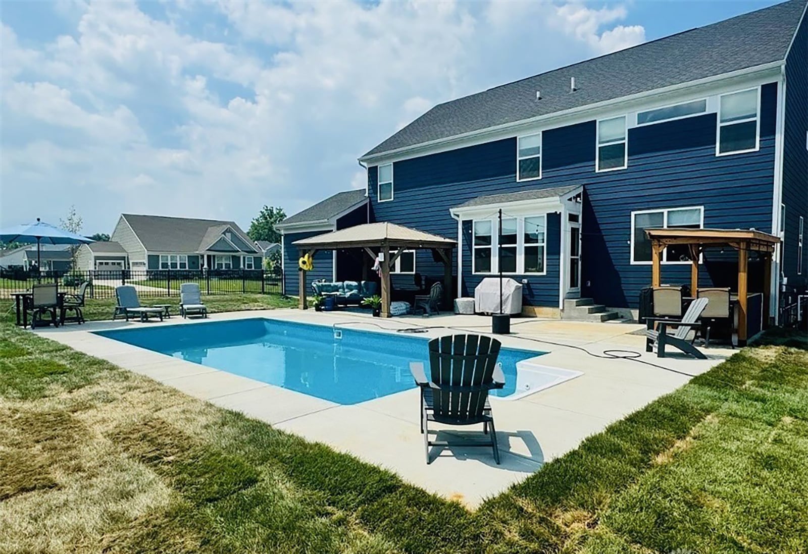 The back of the home features an inground, heated pool with partially covered concrete patio and a pergola covered outdoor kitchen. The backyard is surrounded by a metal fence. CONTRIBUTED