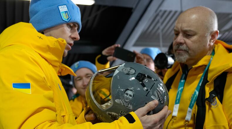 Ukrainian skeleton athlete Vladyslav Heraskevych left, holds his crash helmet at the mixed zone of the sliding center at the 2026 Winter Olympics, in Cortina d'Ampezzo, Italy, Thursday, Feb. 12, 2026. (AP Photo/Alessandra Tarantino)