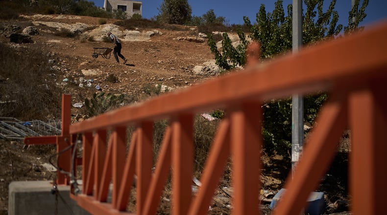 A Palestinian man pushes a wheelbarrow past a closed gate set up by Israeli authorities that blocks an entrance to the West Bank village of Sinjil, Tuesday, Sept. 30, 2025. (AP Photo/Leo Correa)