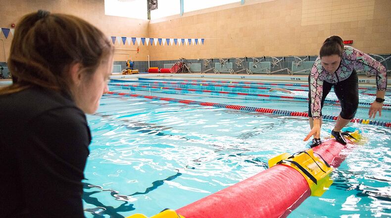Wright-Patterson Air Force Base Life Guard Shelbi Bauer holds a synthetic log in place while Kaley Bartosik, WPAFB Outdoor Recreation director, climbs atop to demonstrate how to log roll. Outdoor Recreation offers two classes a month to teach this up-and-coming sport which is growing in popularity in universities, recreation centers and on military bases, according to Bartosik. (U.S. Air Force photo/John Harrington)