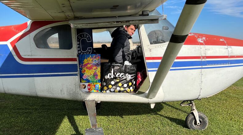 Skydive Greene County pilot Ryan Rogalli smiles while sitting in a red, white, and blue plane loaded with supplies for Kentucky tornado victims.