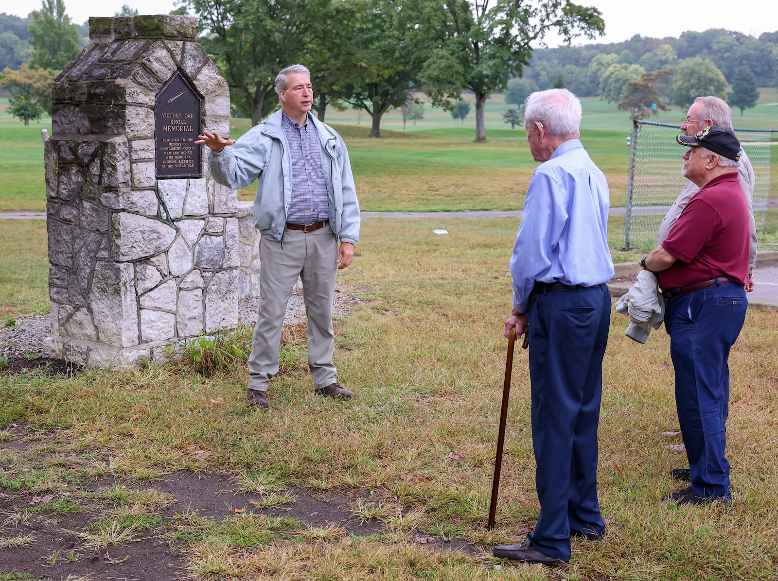 Jim Cunningham (left), an adult leader and former scoutmaster of Scouting America Troop 193, talks about Victory Oak Knoll Memorial as members of the Montgomery County Veterans Service Commission listen on Wednesday, Sept. 24, 2025, in Kettering. Cunningham helped oversee repairs to the memorial, which was damaged in a windstorm last fall. The veterans commission provided funds for repairs. BRYANT BILLING / STAFF