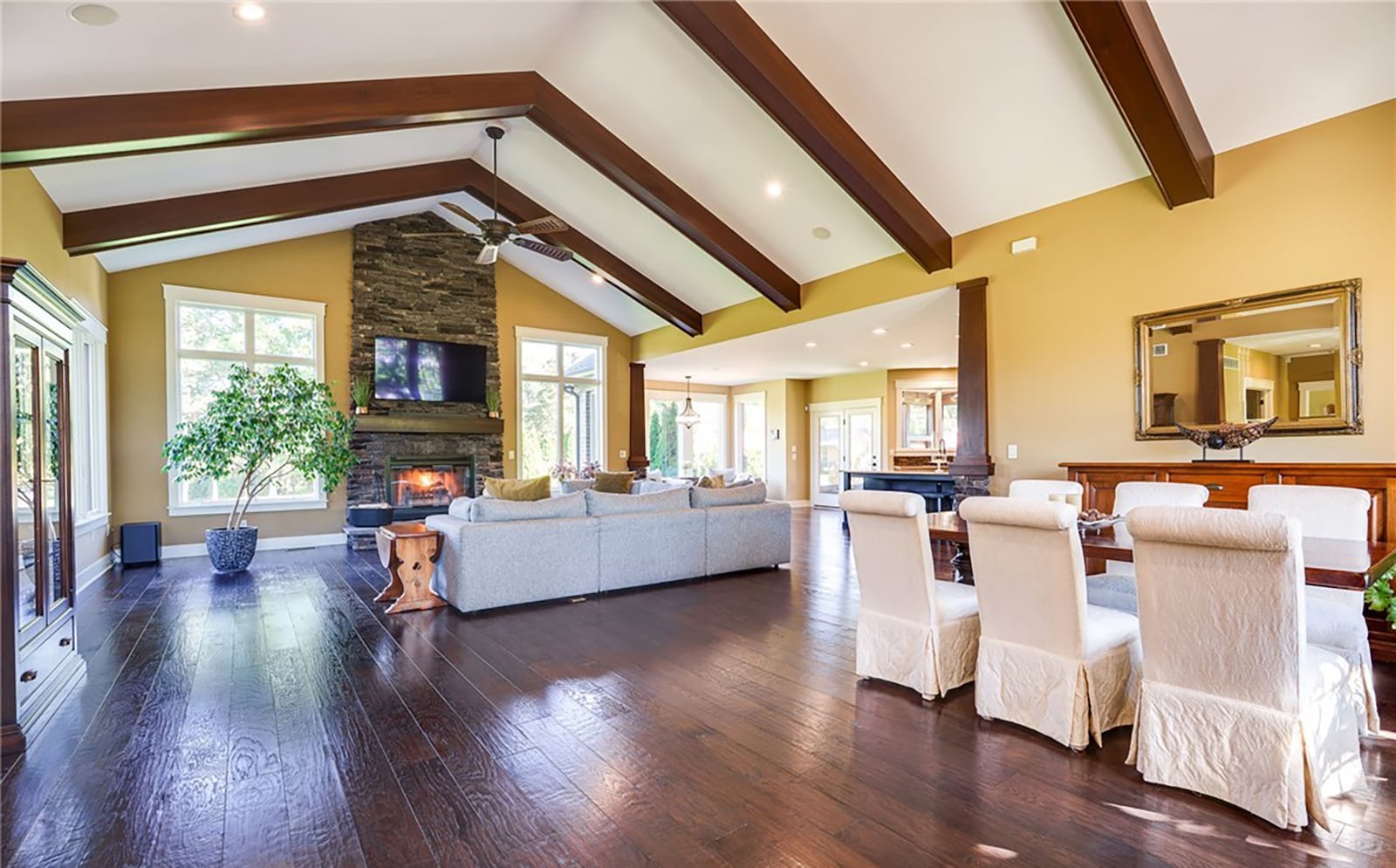The open concept living and dining rooms have wood beamed vaulted ceilings, recessed lighting, a ceiling fan and a floor to ceiling stacked stone fireplace with wood mantel.