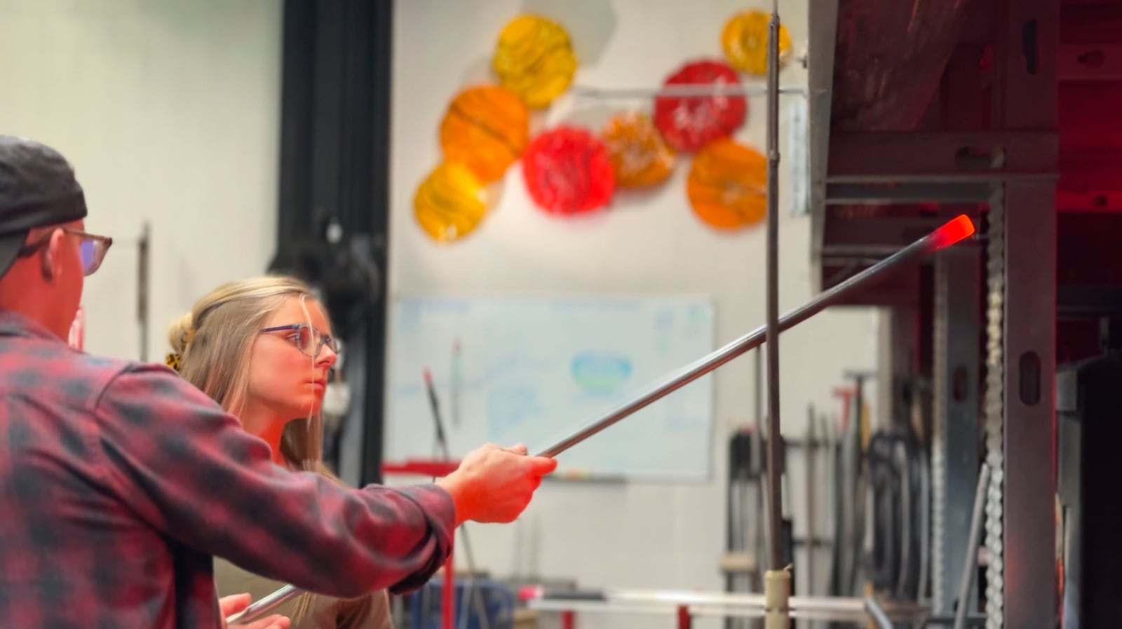 Natalie Jones watches Nyminal Glass owner Dustin Wagner demonstrate glassblowing with a glowing rod of molten glass at his Dayton studio.