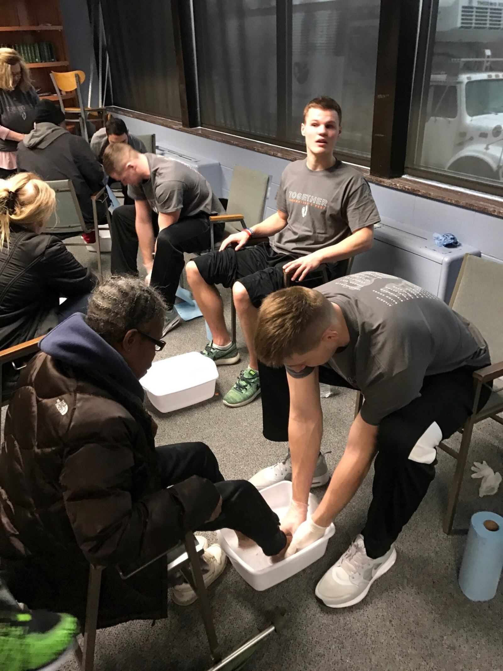 Wright State center Loudon Love washes Marilyn Rockhold’s feet as teammate Grant Benzinger looks on Saturday in East Dayton. TOM ARCHDEACON / CONTRIBUTED