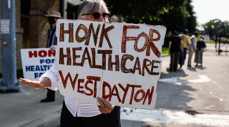 File - Kathleen Galt, from Dayton, along with other protesters carry signs near the site of the now demolished Good Samaritan Hospital on Friday July 23, 2021. Since the site has been replaced by the Premier Health YMCA, members of the Clergy Community Coalition have been trying to get a levy placed on the ballot that would impose a one-mill levy for 10 years for the construction of a new public hospital in west Dayton. JIM NOELKER/STAFF
