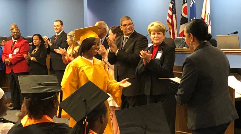 Shataria Blackstone receives her diploma from Thurgood Marshall High School Principal Monica Utley on Tuesday night at a Dayton school board meeting, as other district leaders wait to congratulate her and 25 others. JEREMY P. KELLEY / STAFF