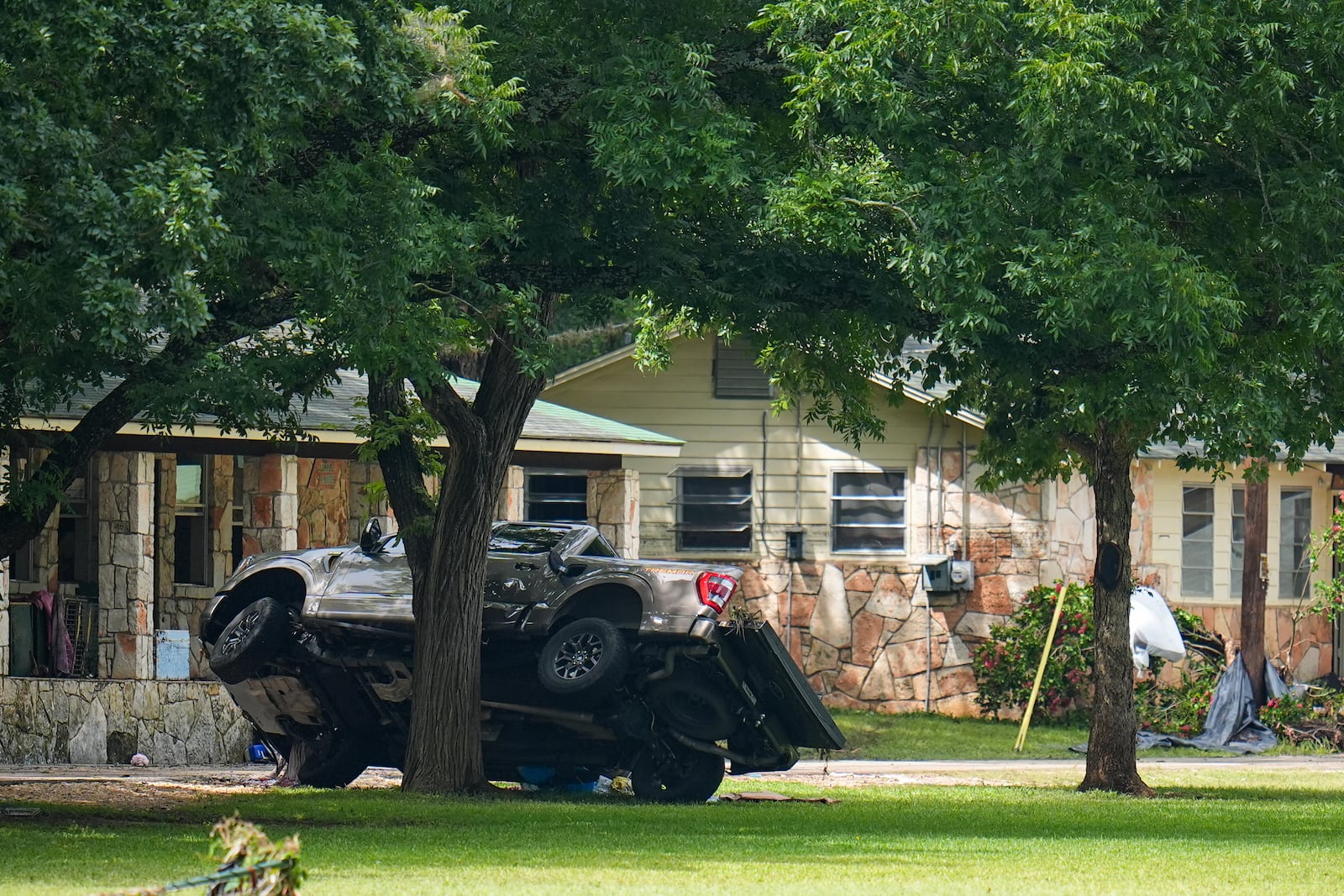 A truck rests on a tree outside sleeping quarters at Camp Mystic along the banks of the Guadalupe River after a flash flood swept through the area Saturday, July 5, 2025, in Hunt, Texas. (AP Photo/Julio Cortez)