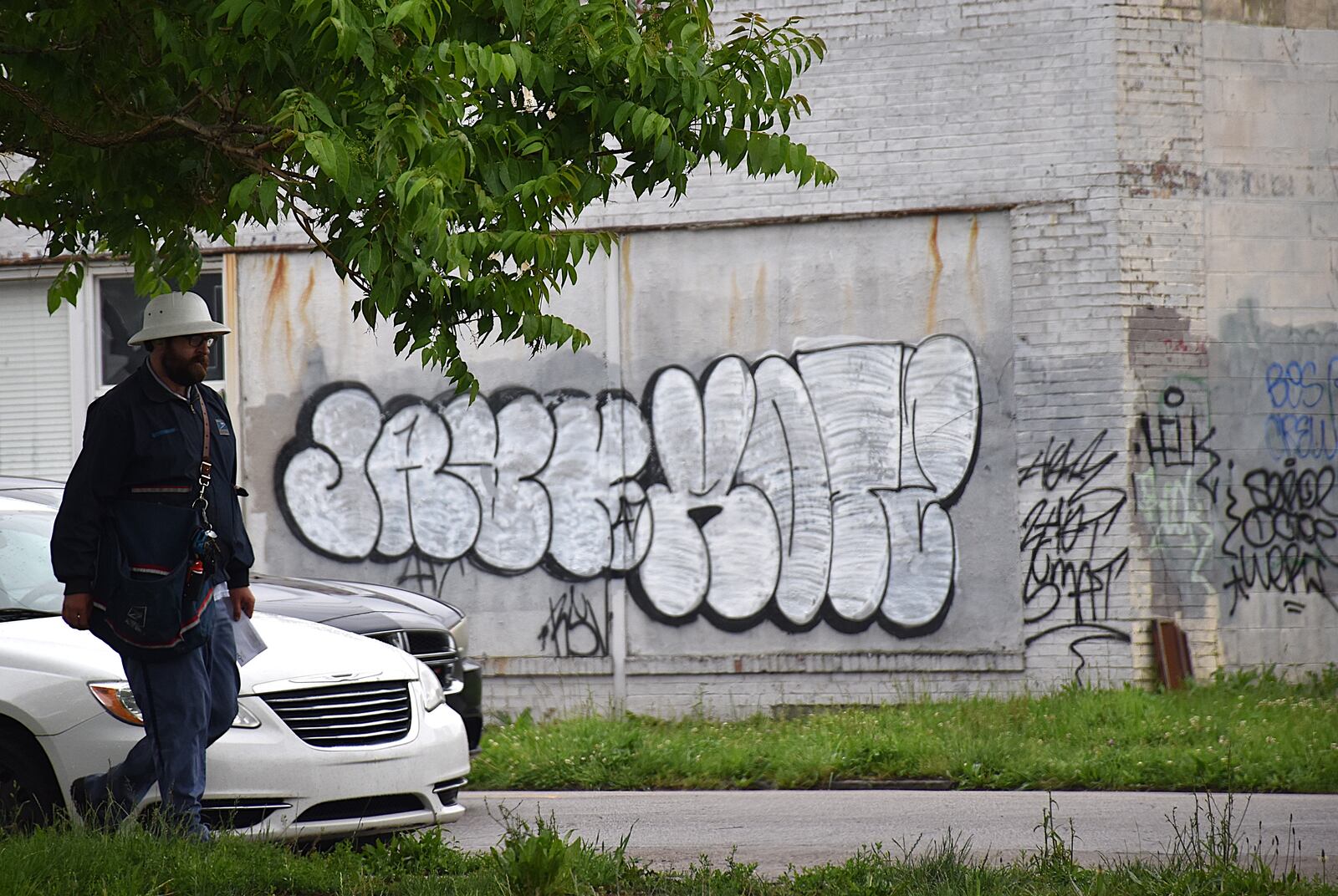 A U.S. Postal Service employee walks down East Third Street in East Dayton by some graffiti on the side of a vacant commercial building. CORNELIUS FROLIK / STAFF