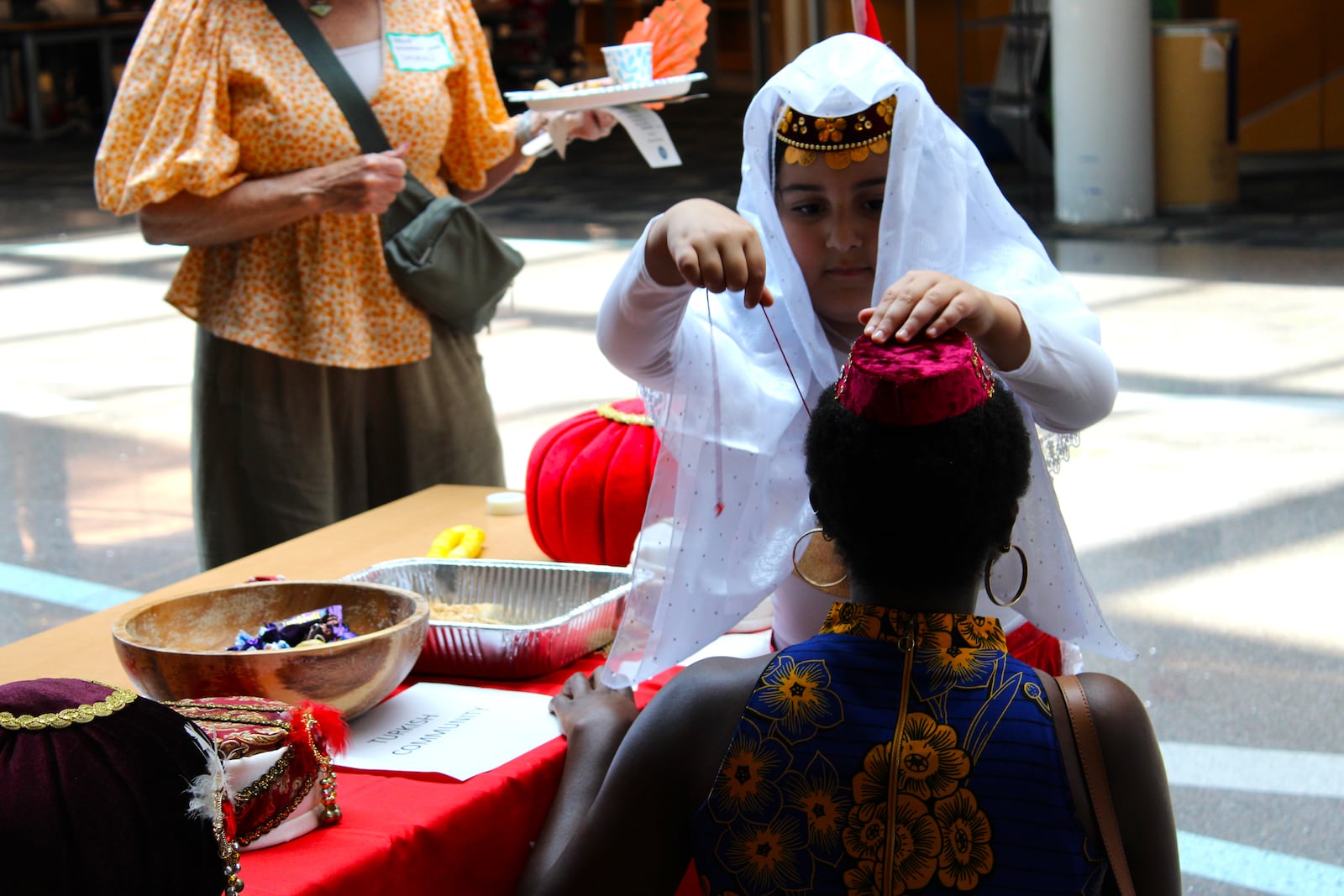 A Turkish girl attaches a traditional head covering, typically used for wedding ceremonies, onto a World Refugee Day attendee's head. STAFF/SYDNEY DAWES