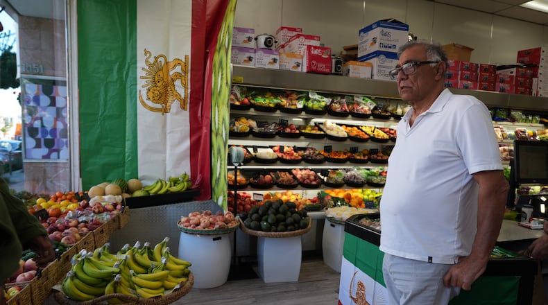Farid, who gave only his first name, from Iran, works at Jordan Market, a Middle Eastern and Persian market along Westwood Boulevard, in the Westwood neighborhood of Los Angeles, pauses next to The Lion and Sun flags, the pre-revolution Iranian national flag, at the heart of the largest Iranian diaspora community in the United States, Monday, March 2, 2026. (AP Photo/Damian Dovarganes)