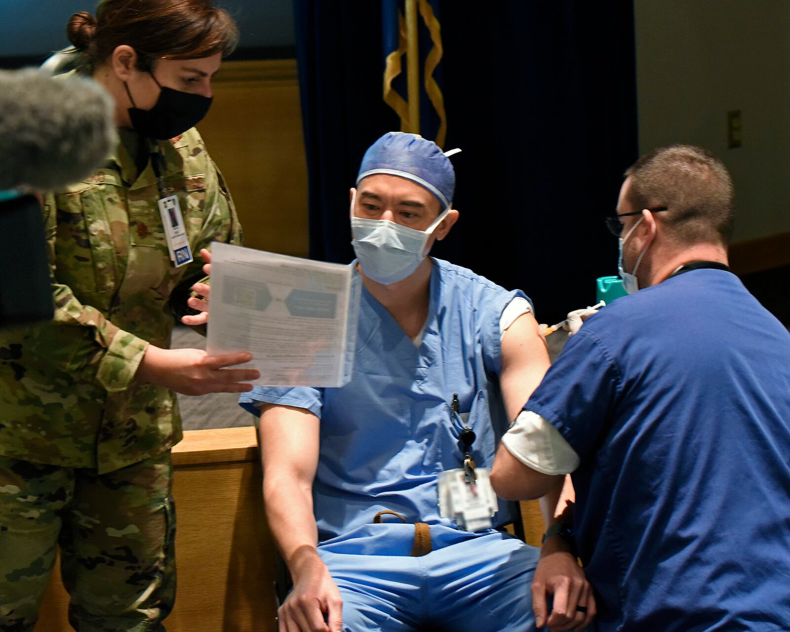 Maj. Richard Brocksmith, an 88th Medical Group nurse anesthetist, listens to instructions from Maj. Holly Holko, 88 MDG medical services flight commander, while receiving the COVID-19 vaccine from Dale Guinther, an 88 MDG nurse, at Wright-Patterson Air Force Base on Jan. 4. Portions of this photo have been altered for security reasons. U.S. AIR FORCE PHOTO/TY GREENLEES