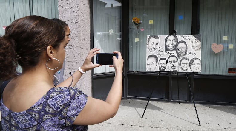 Native Daytonian Christi Colbert takes a picture of a new portrait that is on display in the Oregon District with the faces of the nine shooting victims painted by Abby Kaiser. Colbert was back in town from her current home in Maryland and visited East Fifth Street on Friday afternoon. TY GREENLEES / STAFF