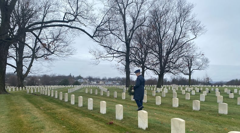 Owen Watkins, a member of the civil air patrol, holds a wreath and walks among the grave markers at Dayton National Cemetery on Saturday, Dec. 18. Eileen McClory / staff