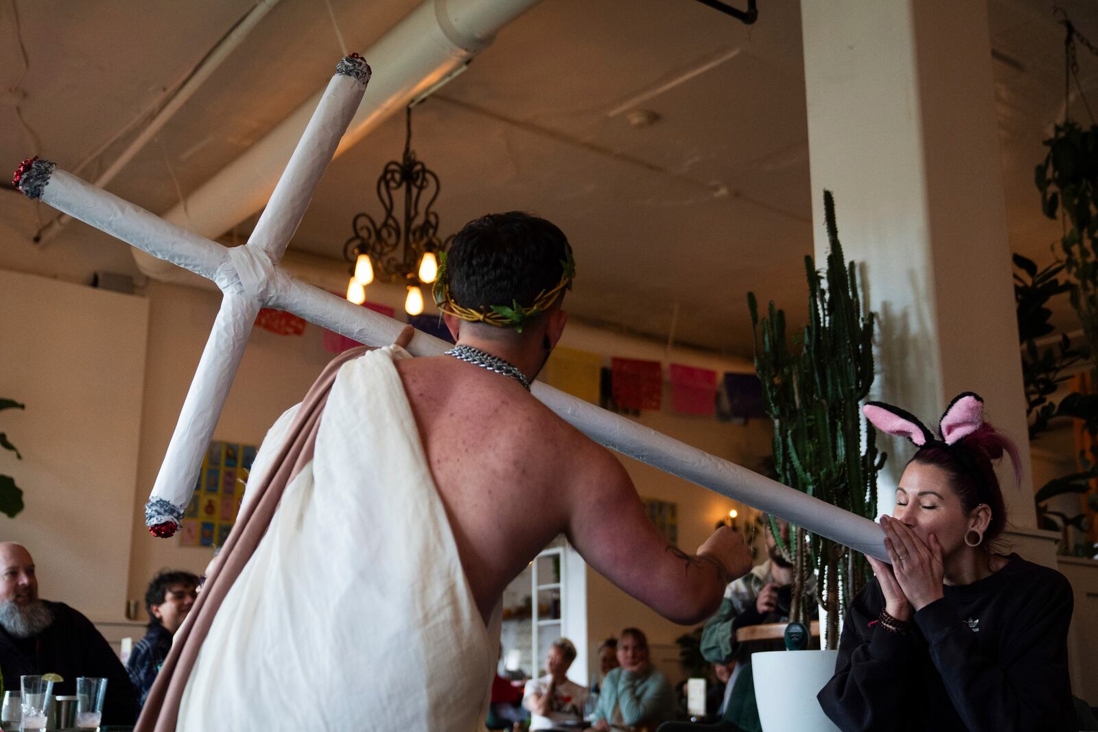 Drag performer Ed Du'Bull, left, holds a cross made to look like lit joints as Krissi Beckel pretends smoke from it during a "blaze and praise" drag brunch at Bar Carlo on Sunday, April 20, 2025, in Portland, Ore. (AP Photo/Jenny Kane)