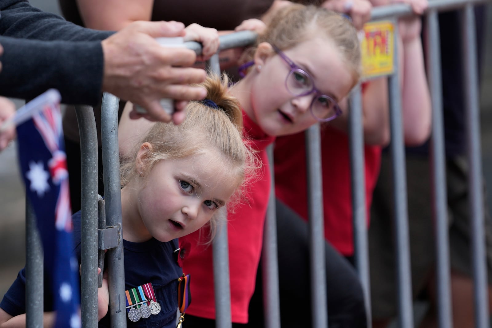 Sage Smith, 5, left, and her six-year-old sister Hazel, peer through a gate while waiting for participants to march by as thousands of people line the street to pay tribute to their war dead during the Anzac Day parade in Sydney, Australia, Friday, April 25, 2025. (AP Photo/Rick Rycroft)