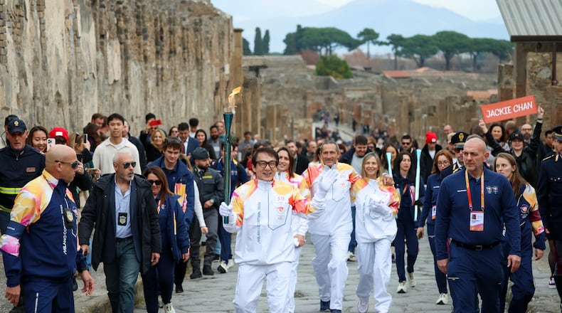 Actor Jackie Chan holds the olympic torch passing through the Archaeological Park in Pompeii, Italy, Monday, Dec. 22, 2025. (Alessandro Garofalo/LaPresse via AP)