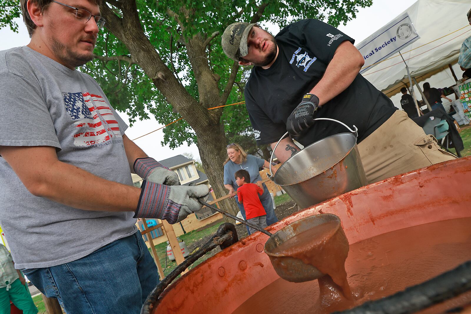 Bruce Bryan, left, and Scott Godby scoop sweet, sticky and piping hot apple butter out of a cauldron Saturday, Oct. 12, 2024 during the Apple Butter Festival in Enon. BILL LACKEY/STAFF